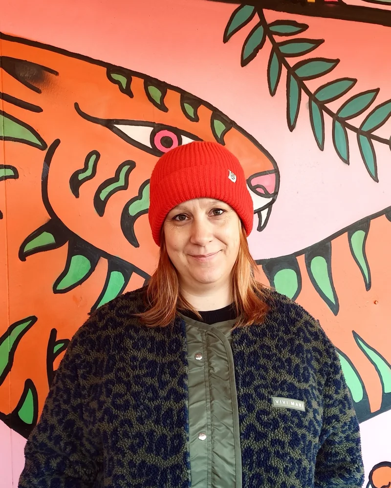 Anja mit roter Mütze und Leo-Jacke vor einem bunten Wandbild